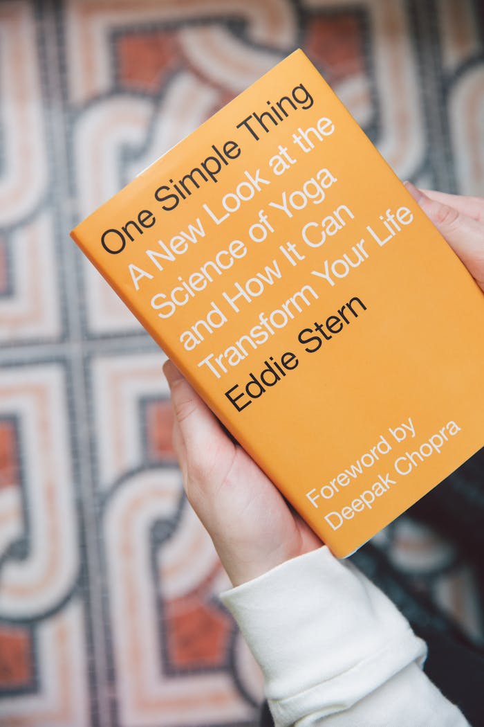 Close-up of hands holding Eddie Stern's book on yoga science, indoors.